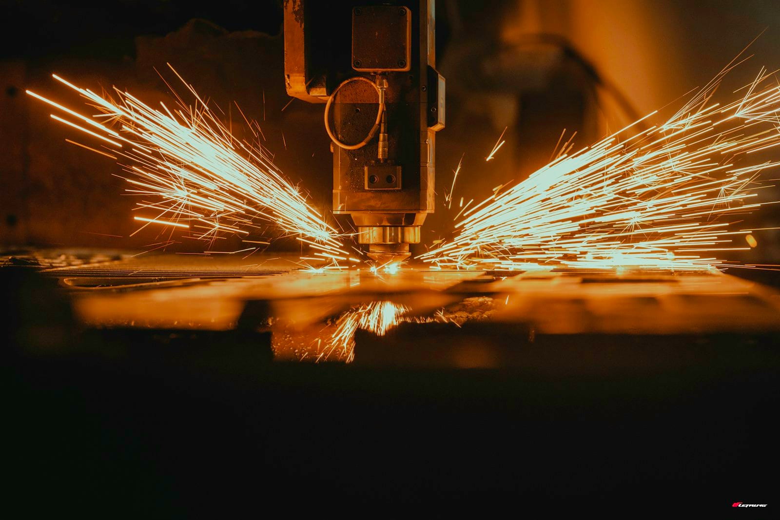 A cutting head throws a fan of sparks as it pierces steel plate on a cutting table